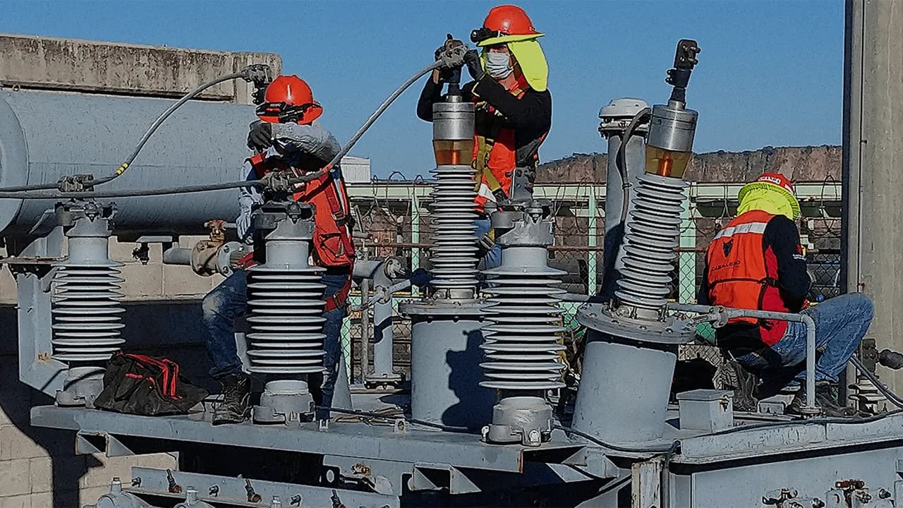 Expertos en sistemas eléctricos con equipo de seguridad dando mantenimiento a una torre de alta tensión